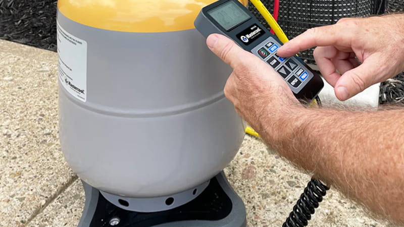 An HVAC technician carefully monitoring a digital refrigerant scale with a recovery tank on it
