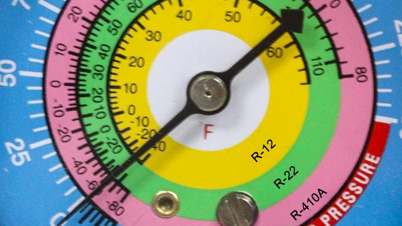 A close-up shot of an analog combo gauge face, showing multiple color-coded scales for R-410A, R-22, and other refrigerants