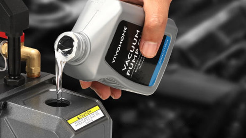 A technician wearing nitrile gloves carefully pours clean, golden-colored vacuum pump oil from a bottle into a pump's fill port