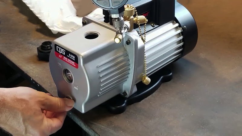 Technician draining old, contaminated vacuum pump oil into a waste container