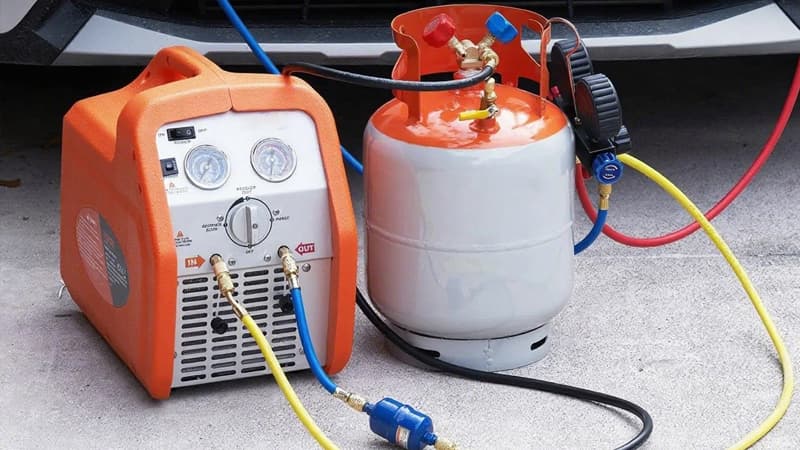 A HVAC technician looking thoughtfully at two different models of refrigerant recovery machines on a workbench