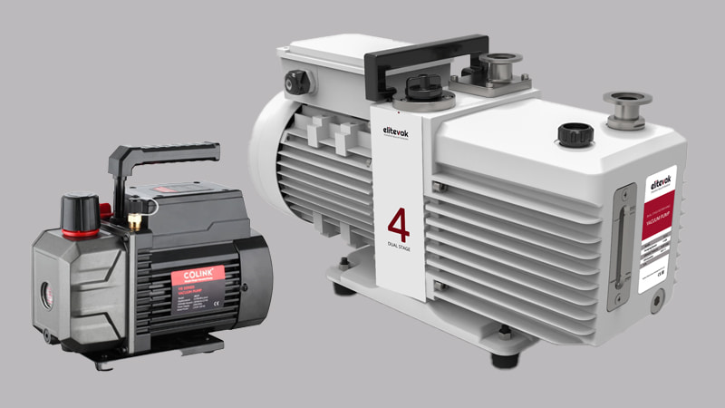 A small, portable vacuum pump sitting next to a large, heavy, cart-mounted industrial vacuum pump, showing the difference in scale