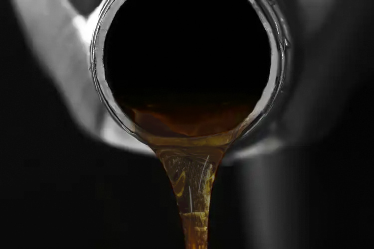 A mechanic draining thick, black, sludgy oil from a vacuum pump into a pan