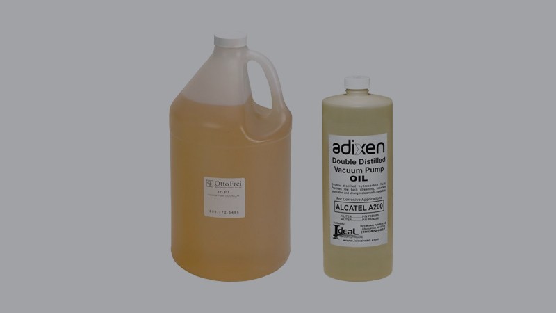 A hand hesitating between two different bottles of vacuum pump oil sitting next to a pump