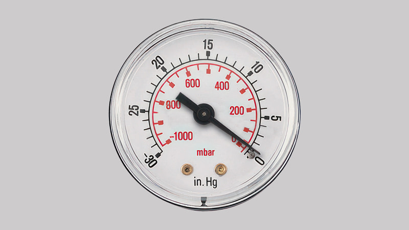A technician looking confused while comparing two different vacuum gauges, one reading in Torr and the other in mbar