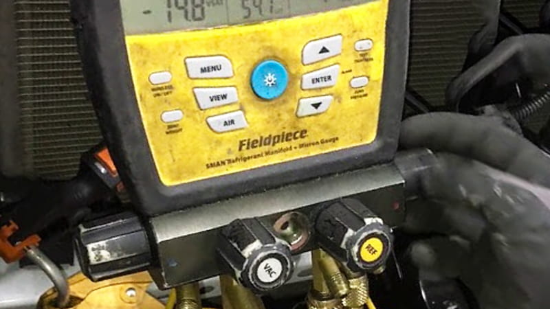 A frustrated HVAC technician in the field looking at the rising numbers on a digital micron gauge