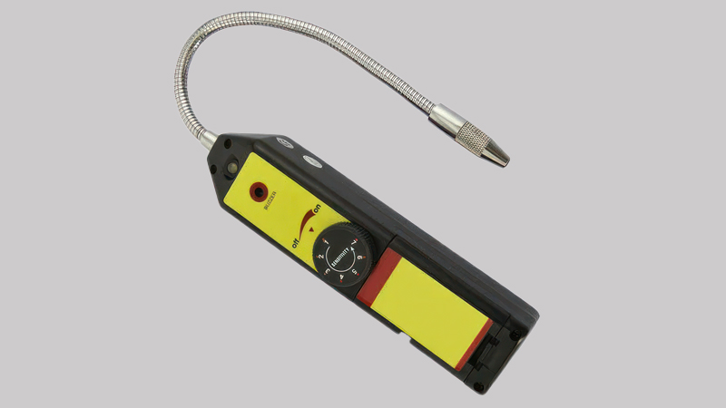 A technician hesitating, holding an old-style halogen leak detector in one hand while looking at the A2L warning sticker on a new HVAC unit