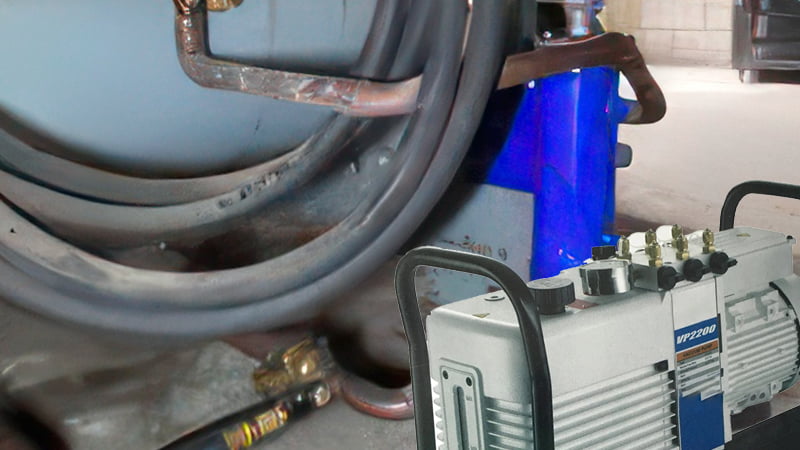 A technician working on a massive commercial rooftop HVAC unit, with a large, cart-mounted vacuum pump connected via thick, large-diameter hoses
