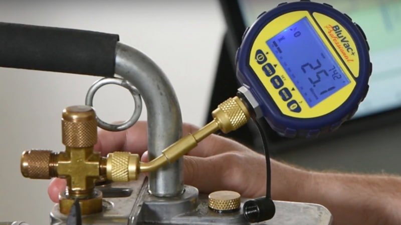 A vacuum pump on a workbench with a micron gauge connected directly to its inlet port, showing a 
