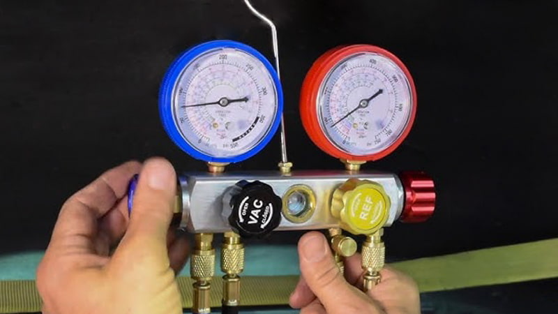 A full set of HVAC manifold gauges with red and blue hoses connected and their ends capped off with brass fittings, ready for testing