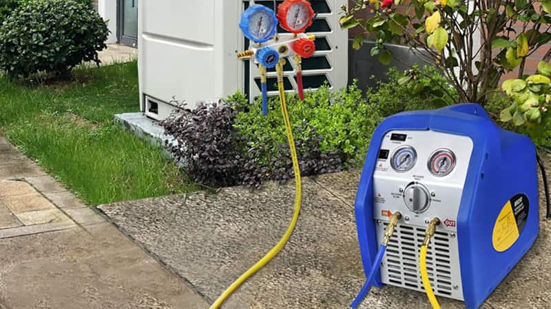 A technician easily carrying a standard-sized recovery machine to a residential ground-level air conditioning unit.