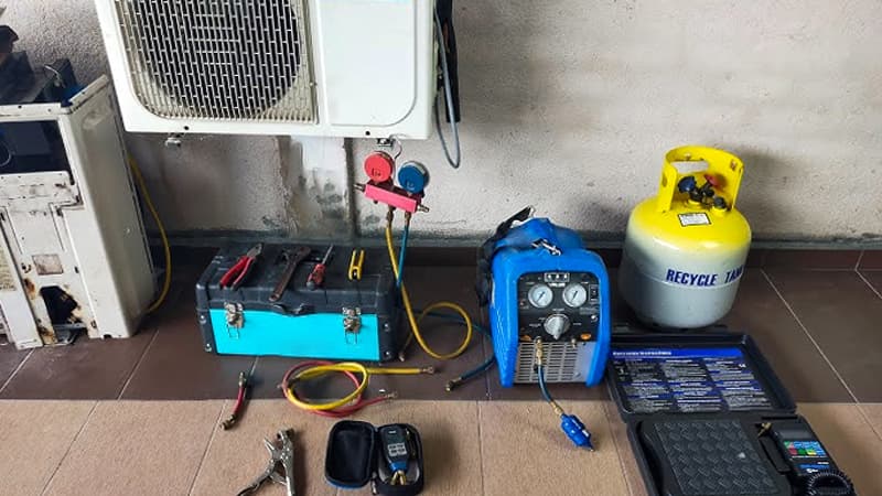 A frustrated HVAC technician on a job site, looking at a recovery machine that has stopped working