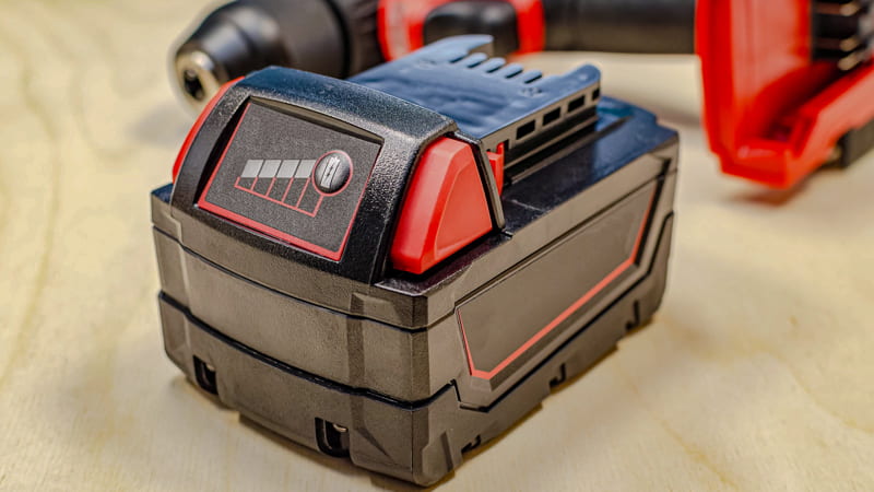 A technician sliding a common power tool battery (e.g., DeWalt or Makita) into an adapter connected to a battery vacuum pump