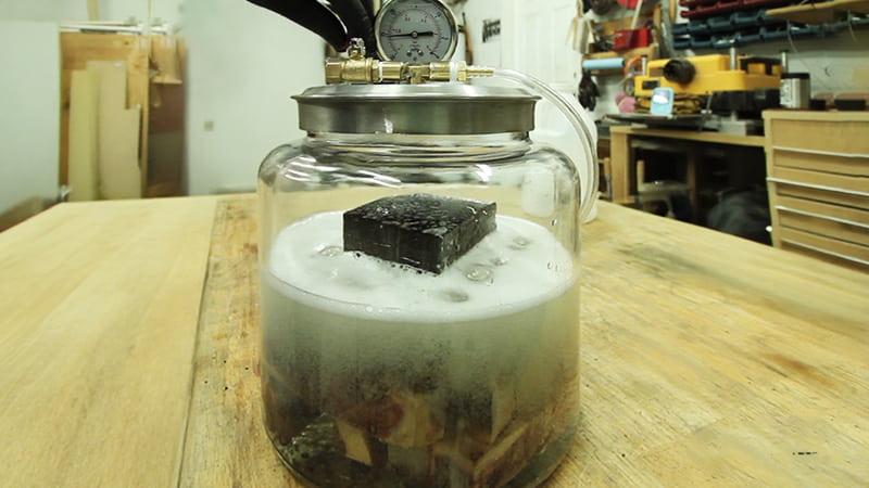 A detailed shot of wood blanks submerged in stabilizing resin (like Cactus Juice) inside a vacuum chamber, with bubbles visibly pouring out of the wood grain