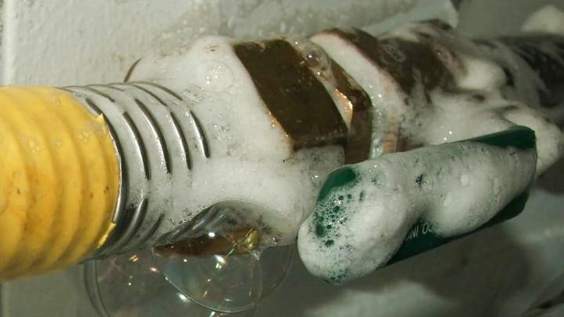 Technician visually inspecting HVAC lines for oil stains with a flashlight